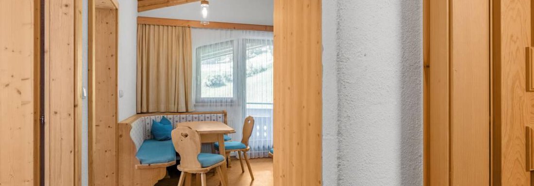 Ein heller Flur mit Holzverkleidung und einer Ecke mit einem Tisch und Stühlen. Hinter einem Fenster ist ein Blick auf die Natur zu sehen. - Garni Nadine - Sölden