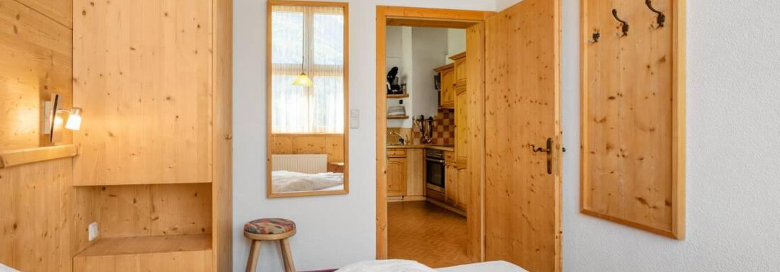 Ein gemütliches Zimmer mit Holzvertäfelung und einem Doppelbett. Die Türen führen in einen weiteren Raum und die Fenster sorgen für viel Tageslicht. - Garni Nadine - Sölden