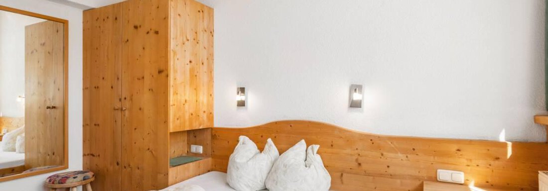 Ein gemütliches Schlafzimmer mit Holzverkleidung und einem großen Bett. Es gibt einen Spiegel und eine moderne Beleuchtung, die eine einladende Atmosphäre schaffen. - Garni Nadine - Sölden