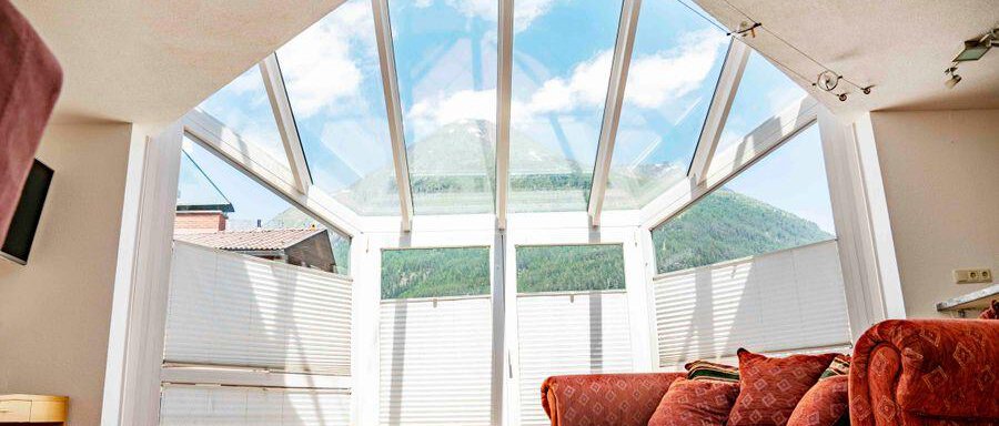 Ein heller Raum mit großen Fensterelementen und Blick auf die Berge. Im Vordergrund steht ein gemütliches Sofa in einem warmen Farbton. - Garni Nadine - Sölden