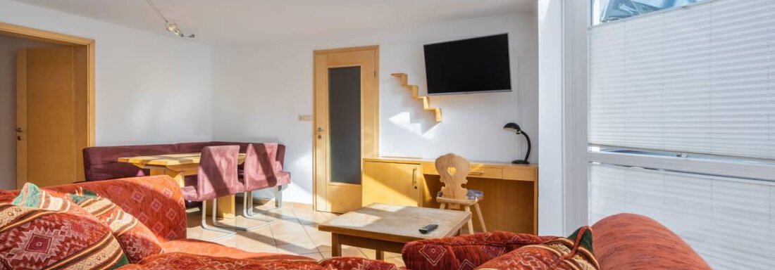 Ein helles Wohnzimmer mit großen Fenstern und modernem Mobiliar. Es gibt eine gemütliche Couch und einen Tisch im Raum. - Garni Nadine - Sölden