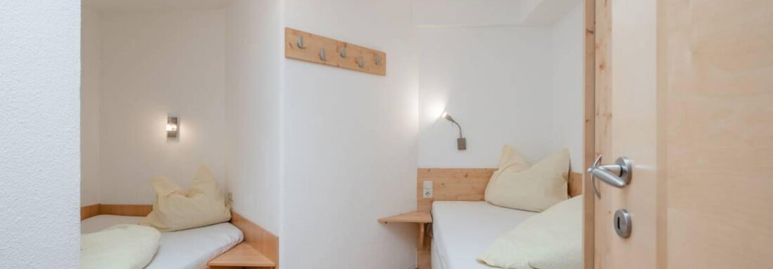 Ein einfaches Zimmer mit zwei Einzelbetten und Holzdetails. Die Wände sind hell, und es gibt eine moderne Deckenlampe. - Garni Nadine - Sölden