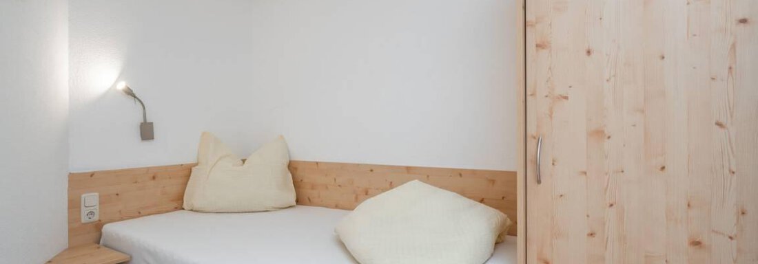 Ein einfaches Zimmer mit hellen Wänden und einem Einzelbett. Es gibt ein Holzregal und einen Kleiderschrank, sowie gemütliche Kissen. - Garni Nadine - Sölden