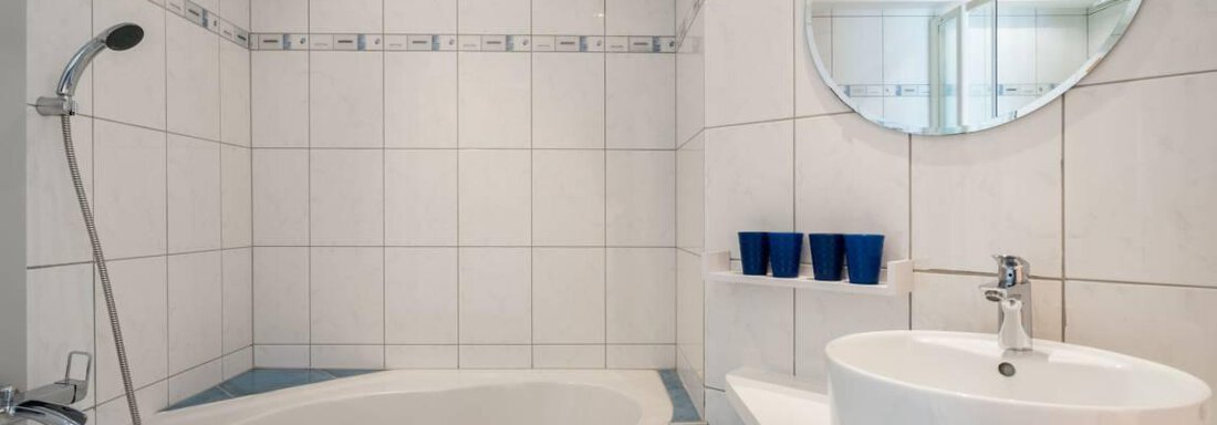 Ein modernes Badezimmer mit einer Badewanne und einem Waschbecken. Die Wände sind hell gefliest und es gibt einen großen Spiegel. - Garni Nadine - Sölden