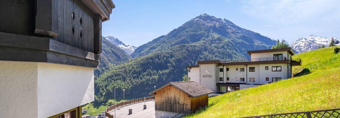 Eine malerische Berglandschaft mit grünen Wiesen und hohen Bergen. Im Vordergrund sind charmante Holzgebäude zu sehen. - Garni Nadine - Sölden