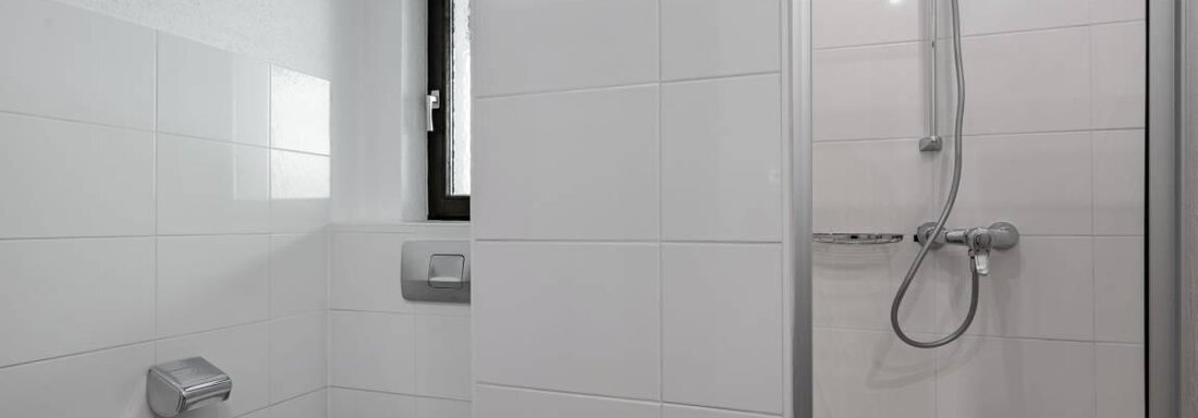 Ein modernes Badezimmer mit einer Dusche und einer Toilette. Die Wände sind mit weißen Fliesen gestaltet und es gibt ein Fenster für Tageslicht. - Garni Nadine - Sölden