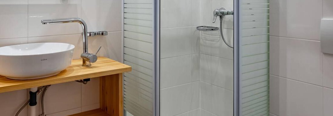Ein modernes Badezimmer mit einer Dusche und einer handgefertigten Holzablage. Die Wände sind hell gefliest und der Waschbecken ist stilvoll gestaltet. - Garni Nadine - Sölden