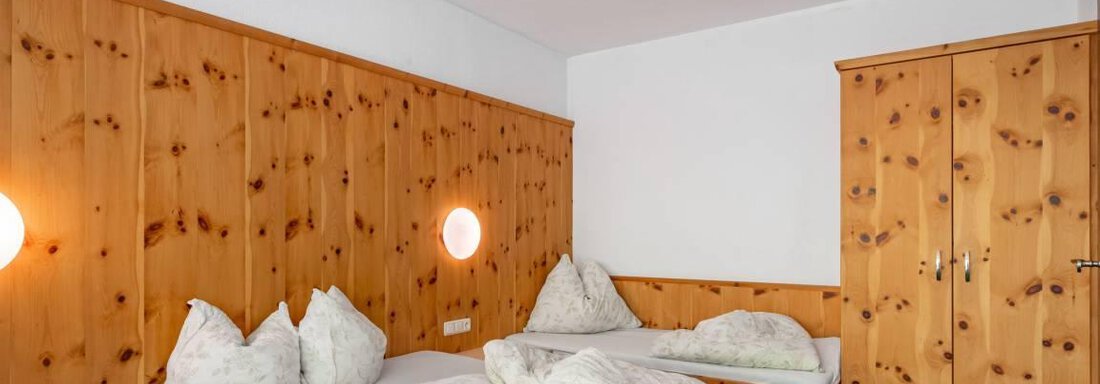 Ein einfaches Schlafzimmer mit Holzvertäfelung. Es gibt zwei Betten und einen Kleiderschrank. - Garni Nadine - Sölden