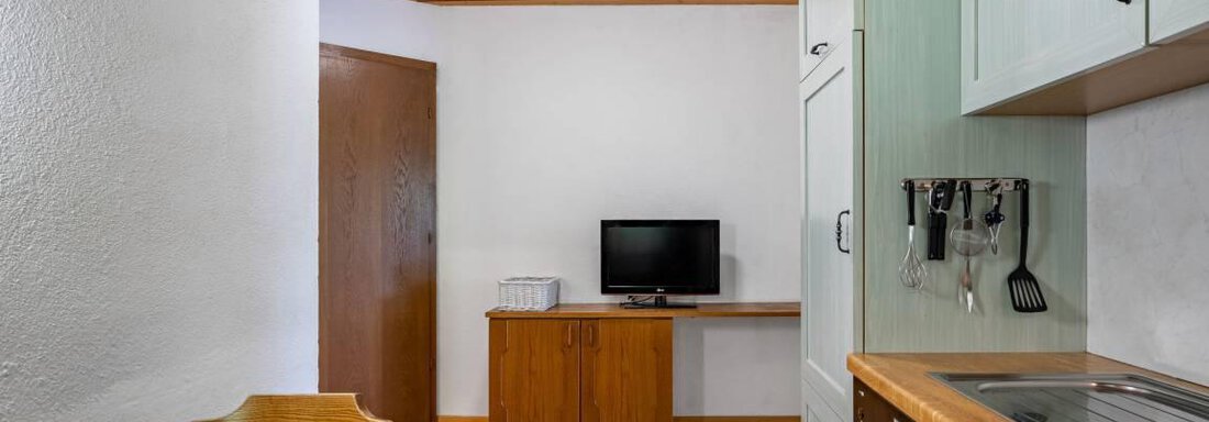 Ein helles, gemütliches Küchenzimmer mit einem Tisch und Stühlen. Die integrierte Küche hat eine moderne Ausstattung und einen Fernseher an der Wand. - Garni Nadine - Sölden