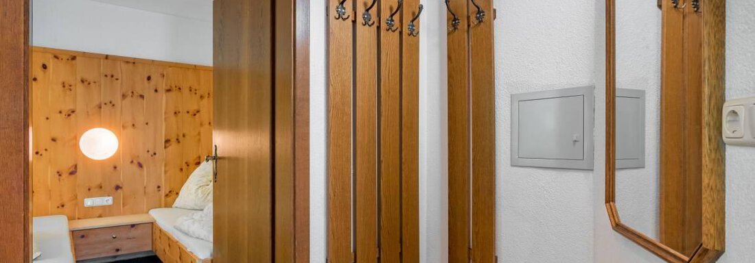 Ein heller Flur mit Holzverkleidung und einem großen Spiegel. An der Wand hängen einige Kleiderhaken, und die Tür führt zu einem Schlafzimmer. - Garni Nadine - Sölden