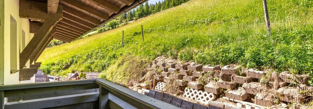Ein Balkon mit Holzverkleidung, der über eine grüne Wiese blickt. Im Hintergrund sind Bäume und ein natürlicher Hang zu sehen. - Garni Nadine - Sölden