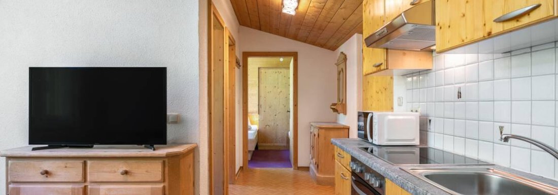 Eine moderne Küche mit Holzschränken und einem großen Fernseher. Der Raum hat eine gemütliche Atmosphäre mit viel natürlichem Licht. - Garni Nadine - Sölden