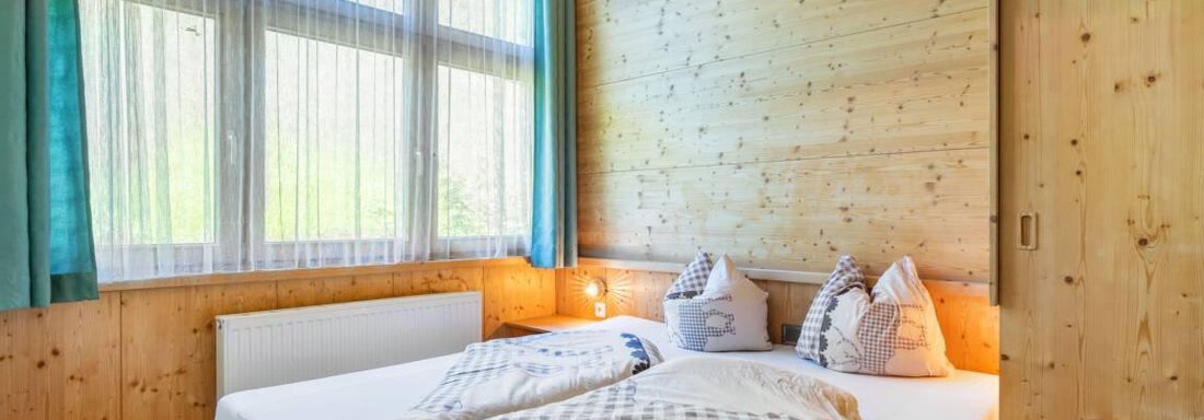 Ein gemütliches Schlafzimmer mit Holzvertäfelung und großen Fenstern. Das Bett ist mit Kissen und einer Decke dekoriert. - Garni Nadine - Sölden