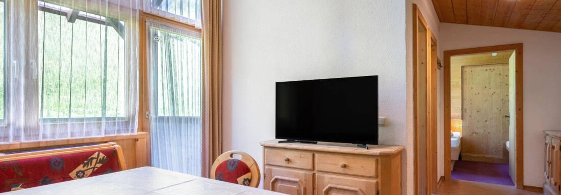 Ein gemütlicher Wohnraum mit einem Tisch und Stühlen. Im Hintergrund steht ein Fernseher und man sieht einen Zugang zu einem weiteren Raum. - Garni Nadine - Sölden