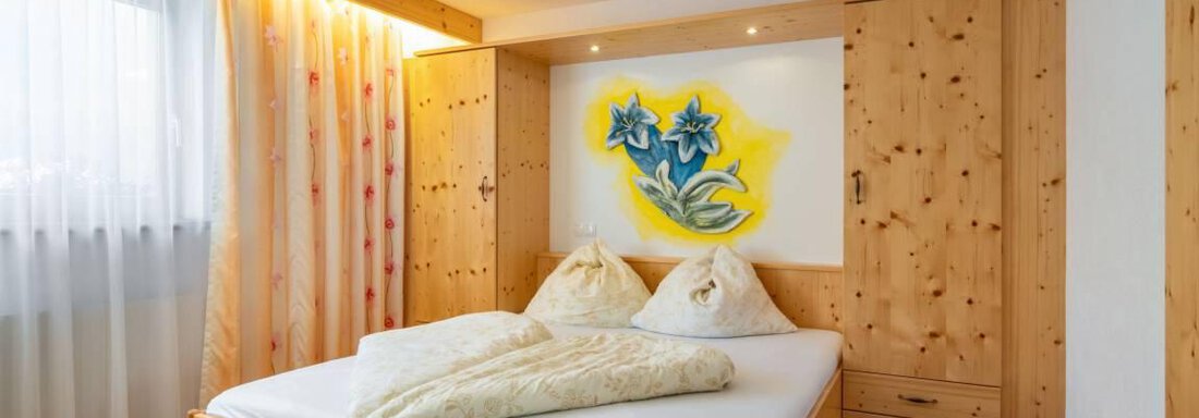 Ein gemütliches Schlafzimmer mit einem Holzbett und einer bunten Wandmalerei. Das Zimmer hat viel natürliches Licht und eine ruhige Atmosphäre. - Garni Nadine - Sölden