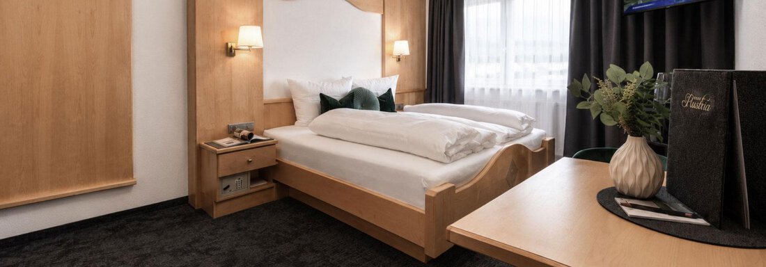 A cozy room with two beds and a modern desk. There is a television and large windows that let in daylight. - Garni Rustica - Sölden