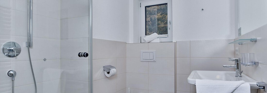 Ein modernes Badezimmer mit Dusche und Toilette. Die Wände sind hell gefliest und es gibt ein großes Fenster. - Gästehaus Bergkristall - Sölden