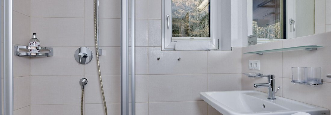 Ein modernes Badezimmer mit Dusche und Waschbecken. Ein Fenster lässt natürliches Licht herein. - Gästehaus Bergkristall - Sölden