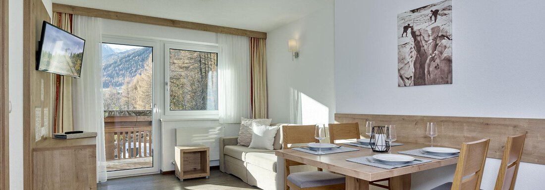 Ein modernes Wohnzimmer mit einem Esstisch und Stühlen. Große Fenster lassen viel Tageslicht herein und bieten einen Blick auf die Berge. - Gästehaus Bergkristall - Sölden