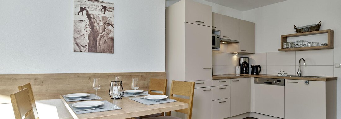 Eine helle, moderne Küche mit einem Essbereich. Der Tisch ist gedeckt und die Einrichtung ist in neutralen Farben gehalten. - Gästehaus Bergkristall - Sölden
