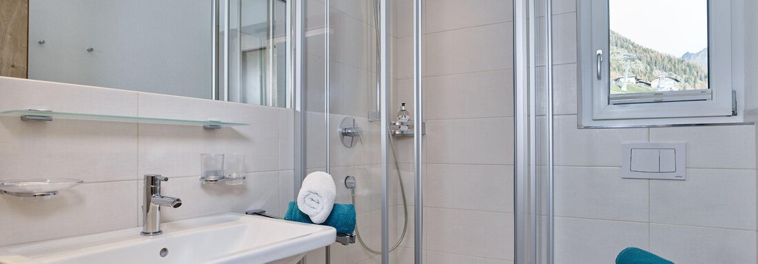 Ein modernes Badezimmer mit einer Dusche und einem Waschbecken. Die sanitären Einrichtungen sind sauber und gut beleuchtet. - Gästehaus Bergkristall - Sölden