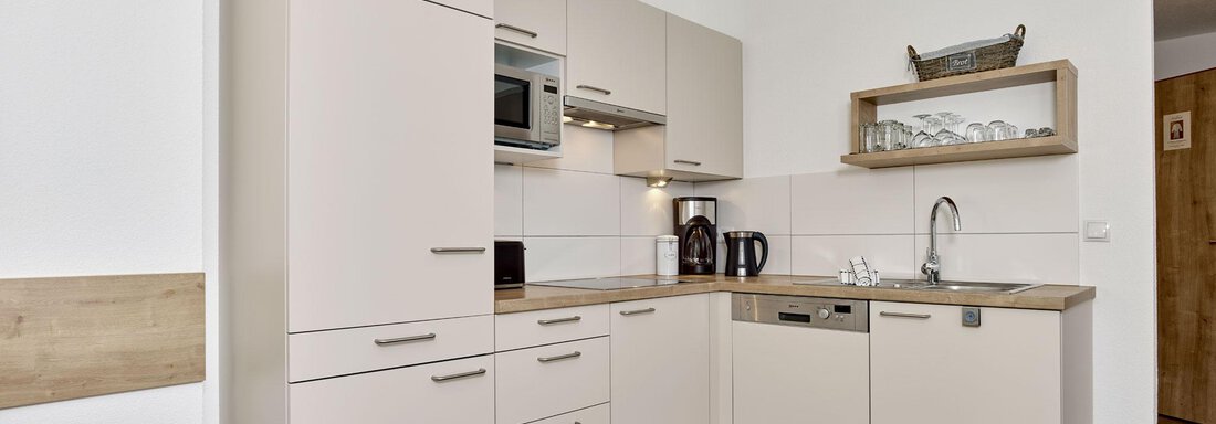 Eine moderne Küche mit hellen Schränken und einer Holzoberfläche. Sie ist funktional eingerichtet und hat verschiedene Geräte wie Mikrowelle und Geschirrspüler. - Gästehaus Bergkristall - Sölden