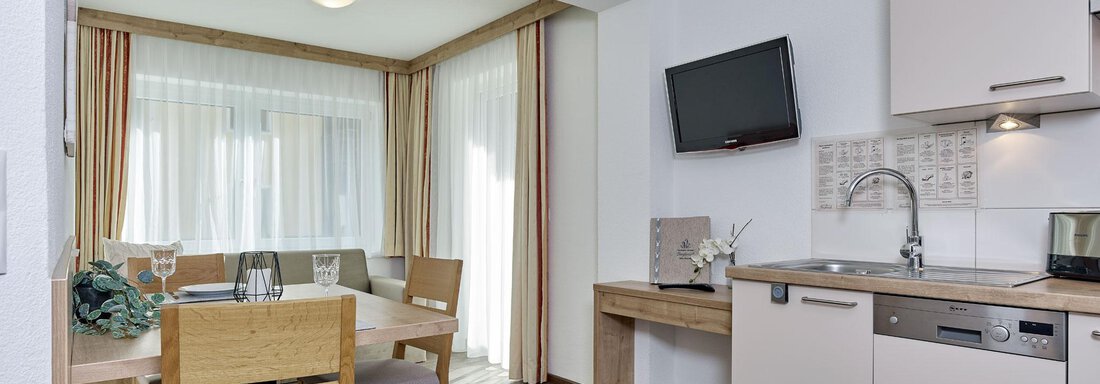 Eine moderne Küche mit einem Esstisch und Stühlen. Großer Fensterbereich sorgt für viel Tageslicht. - Gästehaus Bergkristall - Sölden
