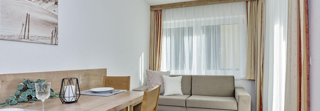 Ein helles Wohnzimmer mit einem Essbereich und einer bequemen Couch. Große Fenster lassen viel Licht herein und schaffen eine einladende Atmosphäre. - Gästehaus Bergkristall - Sölden