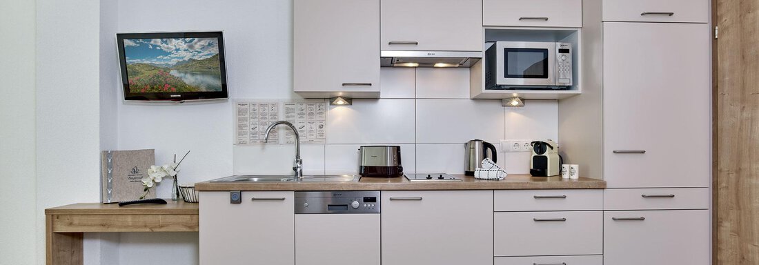 Eine moderne Küche mit hellen Schränken und einem Holzarbeitsplatz. Es gibt Geräte wie einen Kühlschrank, eine Mikrowelle und einen Geschirrspüler. - Gästehaus Bergkristall - Sölden
