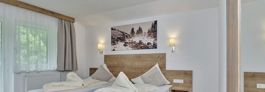 Ein modernes Zimmer mit zwei Einzelbetten und Holzverkleidungen. Die Fenster lassen helles Licht herein und ein dekoratives Bild ziert die Wand. - Gästehaus Bergkristall - Sölden