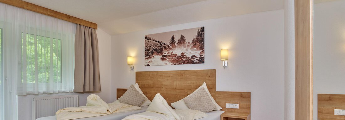Ein helles und modernes Schlafzimmer mit zwei Einzelbetten. Die Wände sind in neutralen Farben gehalten, und ein großes Fenster lässt viel Licht herein. - Gästehaus Bergkristall - Sölden