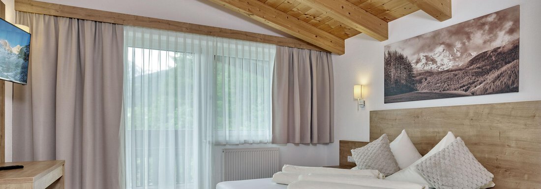 Ein modernes Zimmer mit Holzelementen und einer gemütlichen Atmosphäre. Es bietet ein großes Bett, einen Schreibtisch und ein Fenster mit Blick auf die Natur. - Gästehaus Bergkristall - Sölden