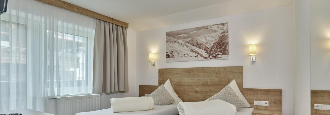 Ein gemütliches Hotelzimmer mit zwei Einzelbetten und modernem Holzdesign. Große Fenster sorgen für viel Tageslicht und eine einladende Atmosphäre. - Gästehaus Bergkristall - Sölden