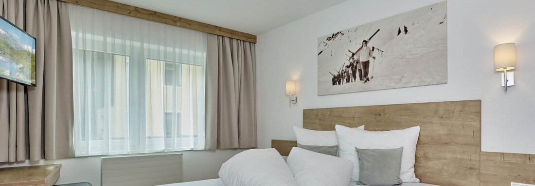 Ein modernes Schlafzimmer mit einem großen Bett und Holzdetails. An der Wand hängt ein Bild von Schnee und Bergen. - Gästehaus Bergkristall - Sölden