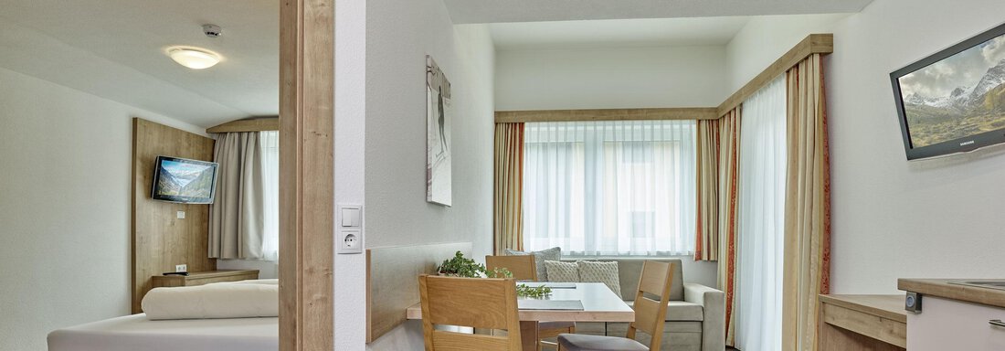 Ein modernes Zimmer mit einem Bett, einem Tisch und Stühlen. Helle Fenster lassen viel Licht herein und schaffen eine einladende Atmosphäre. - Gästehaus Bergkristall - Sölden