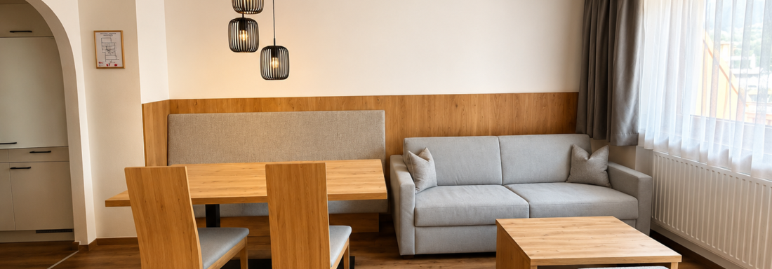 A modern living room with a cozy sofa, a table, and wooden chairs. 

Large windows let in plenty of light and create an inviting atmosphere. - Gästehaus Europa - Sölden