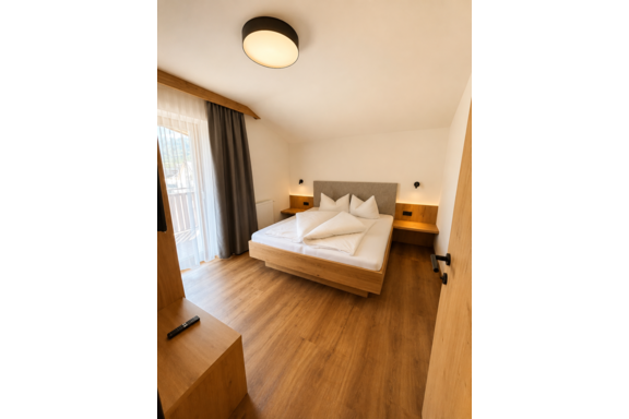 A modern bedroom with a large bed and wooden floor. Large windows provide plenty of natural light. - Gästehaus Europa - Sölden