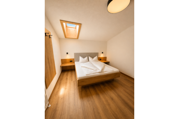 The image shows a modern bedroom with a comfortable bed and warm wooden flooring. A skylight provides natural light and a cozy atmosphere. - Gästehaus Europa - Sölden