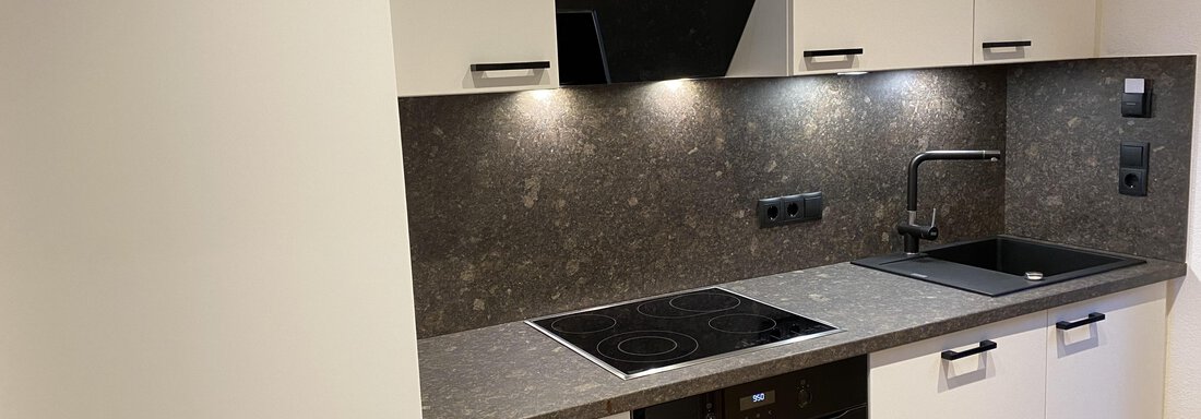 A modern kitchen with white cabinets and a dark countertop. The kitchen features a stove, an oven, and a sink, all in an elegant design. - Gästehaus Europa - Sölden