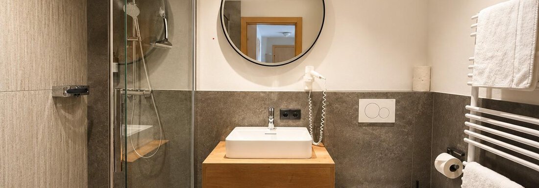 A modern bathroom with a glass shower and a wooden sink. The walls are in neutral colors and there are fresh towels. - Gästehaus Europa - Sölden