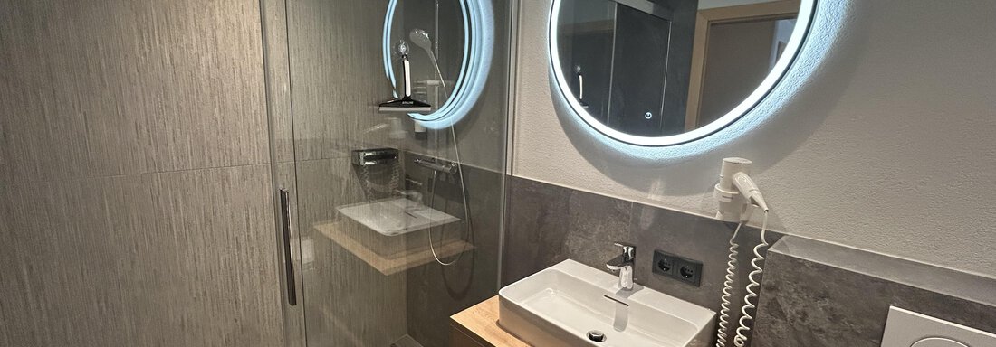 A modern bathroom with a glass shower and a stylish sink. Illuminated mirrors complete the elegant design. - Gästehaus Europa - Sölden