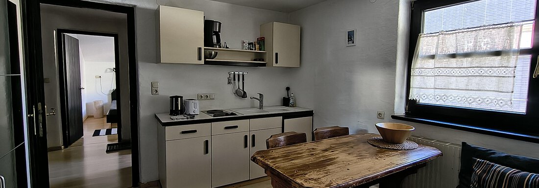 A modern kitchen with a wooden table and chairs. Large windows provide plenty of daylight. - Gästehaus Hermann Arnold - Sölden