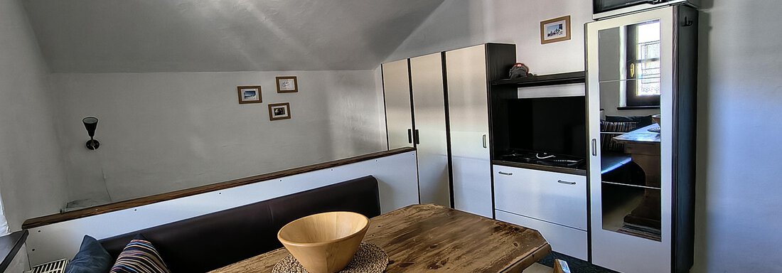 A cozy living kitchen with a wooden table and chairs. On the left side, there is a sofa and a kitchenette. - Gästehaus Hermann Arnold - Sölden