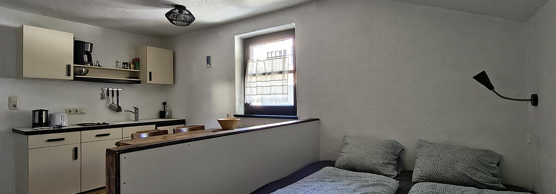 A simple room with two beds and a small kitchenette. Light comes in through a window and there is a colorful rug on the floor. - Gästehaus Hermann Arnold - Sölden