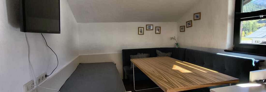 A cozy room with a large table and a sitting area. A television is hung on the wall and there are some picture frames. - Gästehaus Hermann Arnold - Sölden