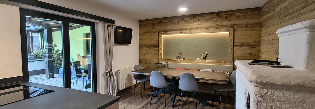 A modern furnished room with a dining area and large windows. The wood look and soft lighting create a cozy atmosphere. - Gästehaus Hermann Arnold - Sölden