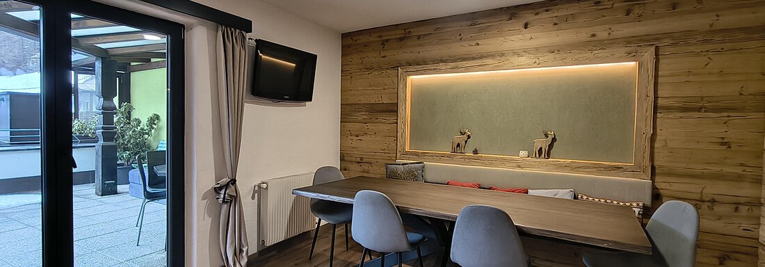 A modern room with a large table and comfortable chairs.  
Large windows provide a view of the outdoor area. - Gästehaus Hermann Arnold - Sölden