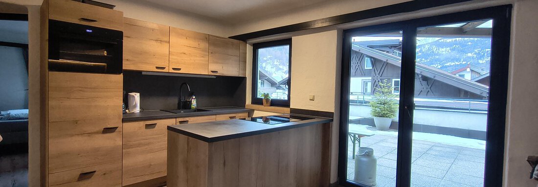 Modern kitchen with wooden shelves and a large window. The room is bright and inviting. - Gästehaus Hermann Arnold - Sölden