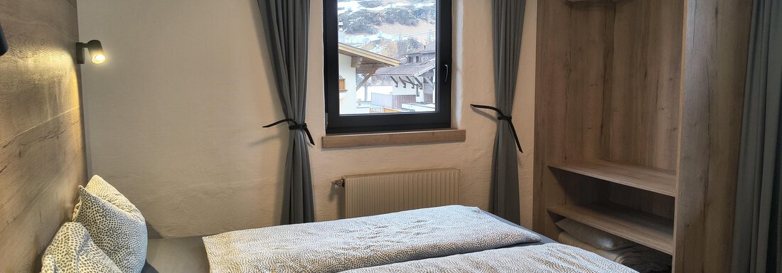 A modern room with two beds and a warm wooden ceiling. The room has a window with views of the mountains and an open wardrobe. - Gästehaus Hermann Arnold - Sölden