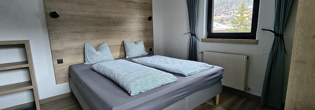 A modern bedroom with a double bed and wooden details. Large windows let in plenty of light and offer a view of nature. - Gästehaus Hermann Arnold - Sölden